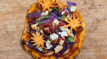 En pizza med frugt og grøntsager på i orange og lilla nuancer.